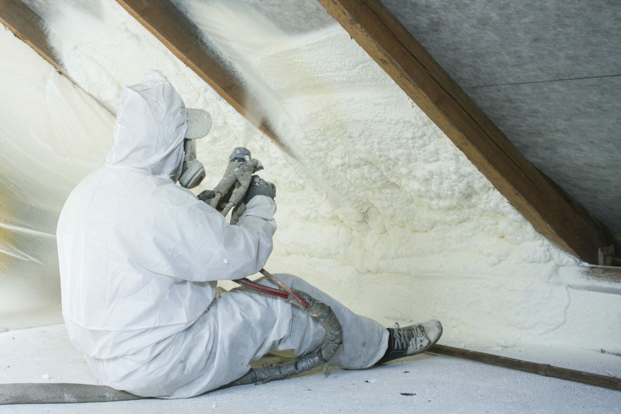 spray polyurethane foam for roof - technician spraying foam insulation using plural component gun for polyurethane foam, inside